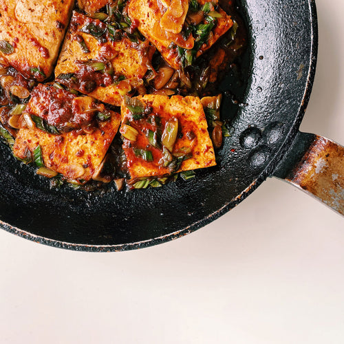 Spicy Braised Tofu in a cast iron skillet with a spicy White Mausu Black Bean Ketchup and caramelised onions.